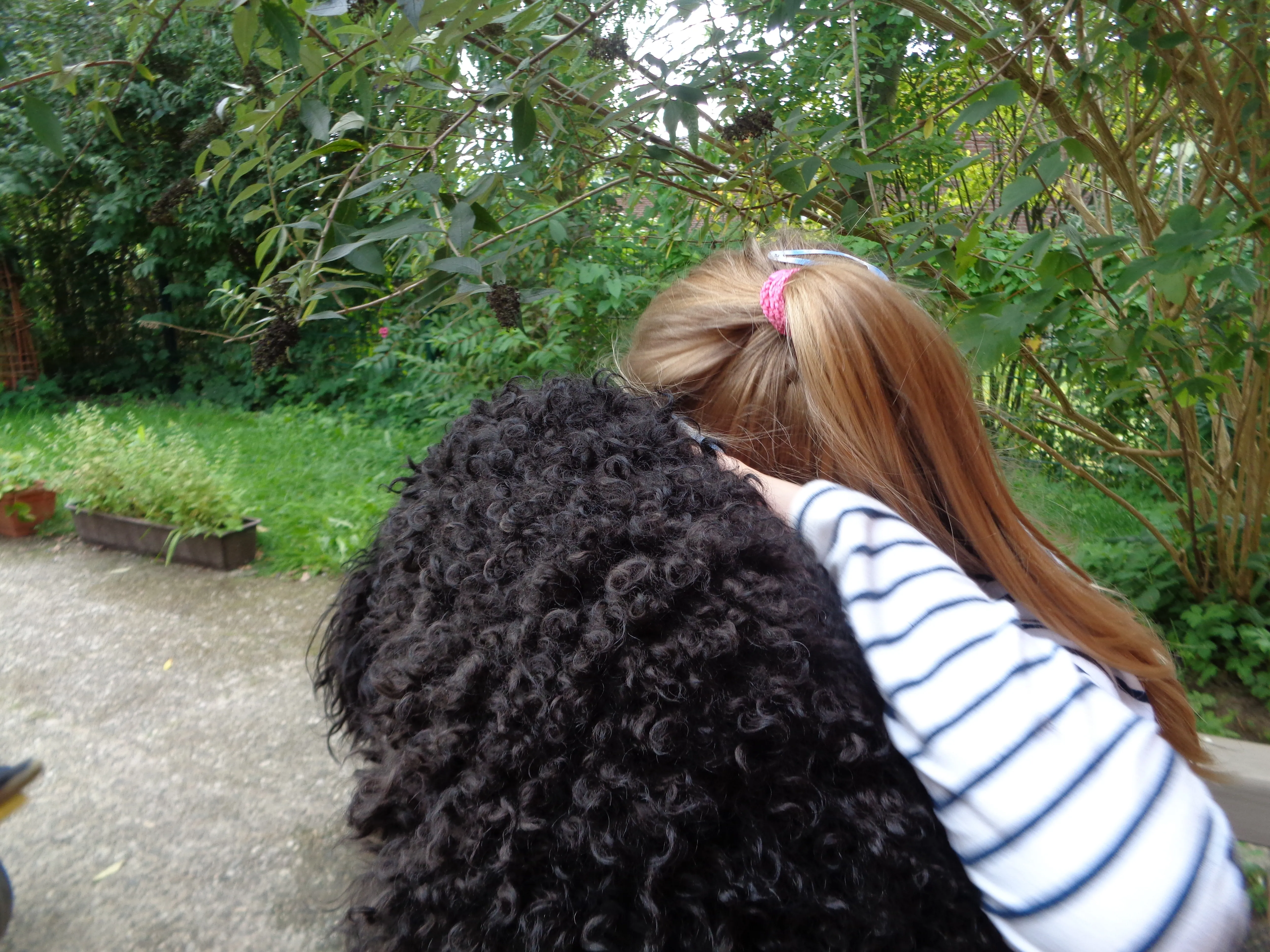 Mädchen umarmt einen großen, lockigen schwarzen Hund im Freien.