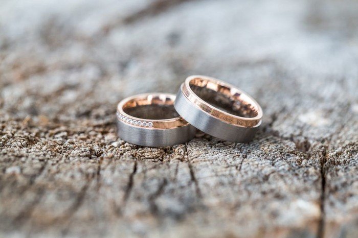  Zwei Eheringe, einer mit Diamanten, auf texturiertem Holzuntergrund.