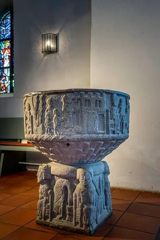 Borby Romanisches Taufbecken mit detaillierten figürlichen Schnitzereien im Kircheninneren.