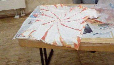 Weißes T-Shirt mit orangefarbenem Spiral-Batikeffekt auf Zeitungspapier.