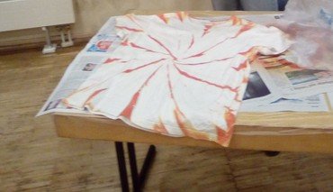 Weißes T-Shirt mit orangefarbenem Spiral-Batikeffekt auf Zeitungspapier.