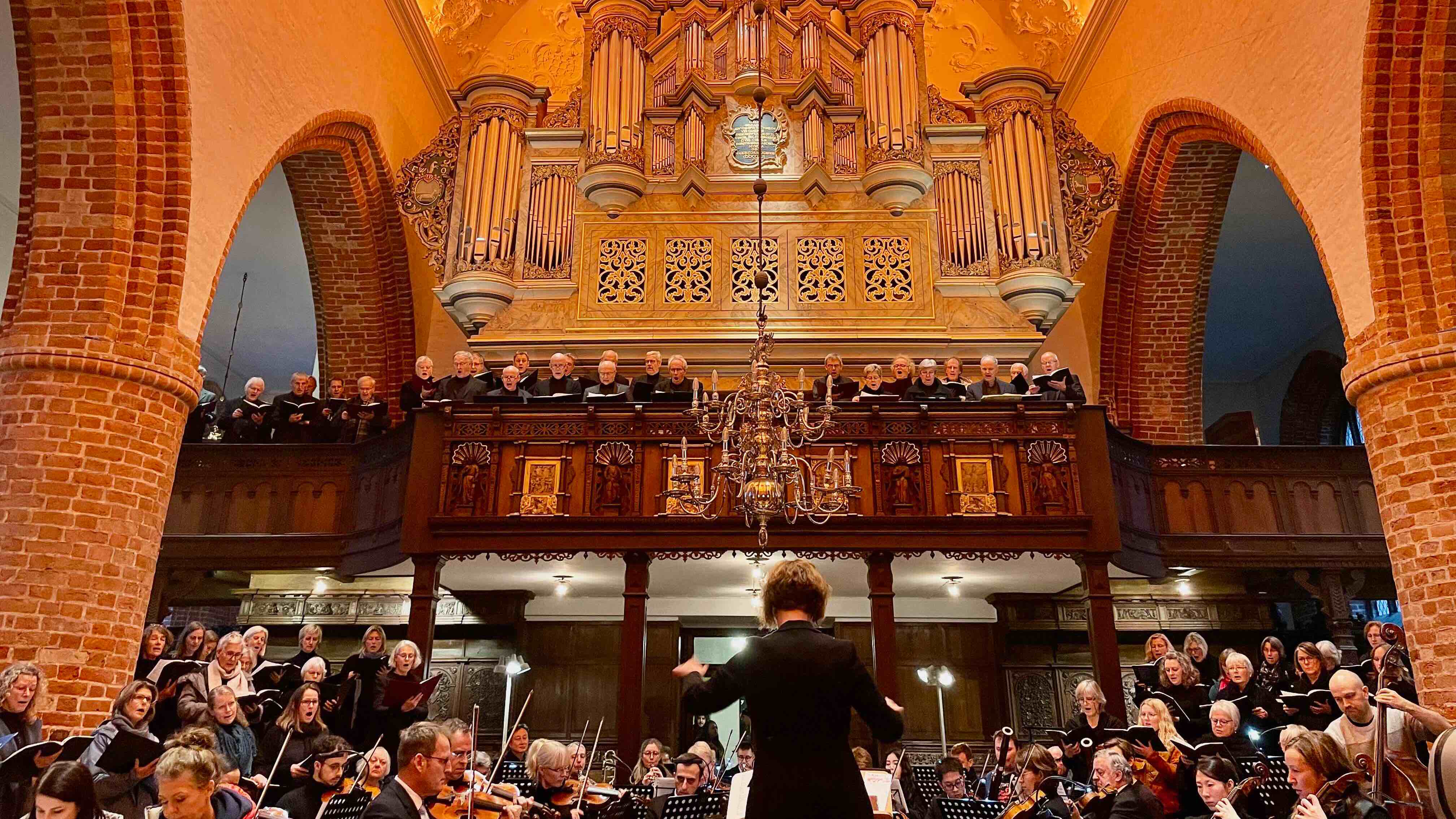 Chor und Orchester musizieren unter einer großen Kirchenorgel.