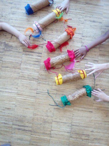 Kinderhände greifen nach verzierten Pappröhren auf einem Fußboden.