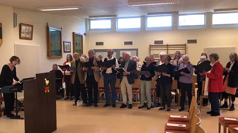 Erwachsenenchor singt drinnen, begleitet von einer Keyboardspielerin.