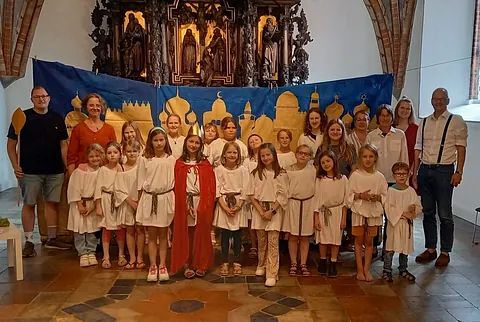 Gruppe Kinder und Erwachsene in Kostümen vor einem Kirchenaltar.