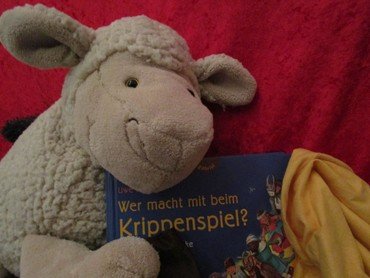 Stoffschaf-Spielzeug lehnt an einem deutschen Weihnachtsbuch.